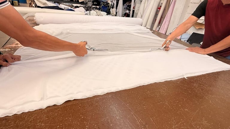 Two people laying out white fabric on a cork surface with clothing visible in the background