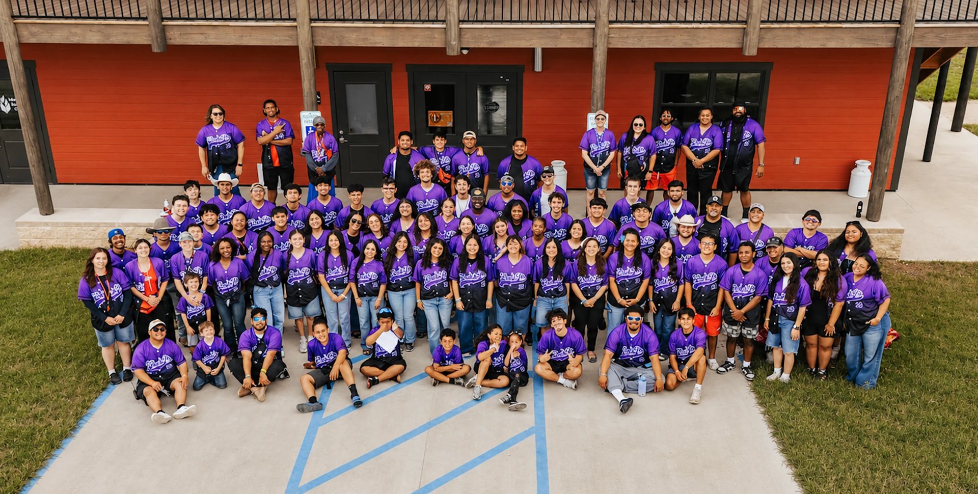 Large group of people wearing purple shirts posing for a photo outside a building with red walls