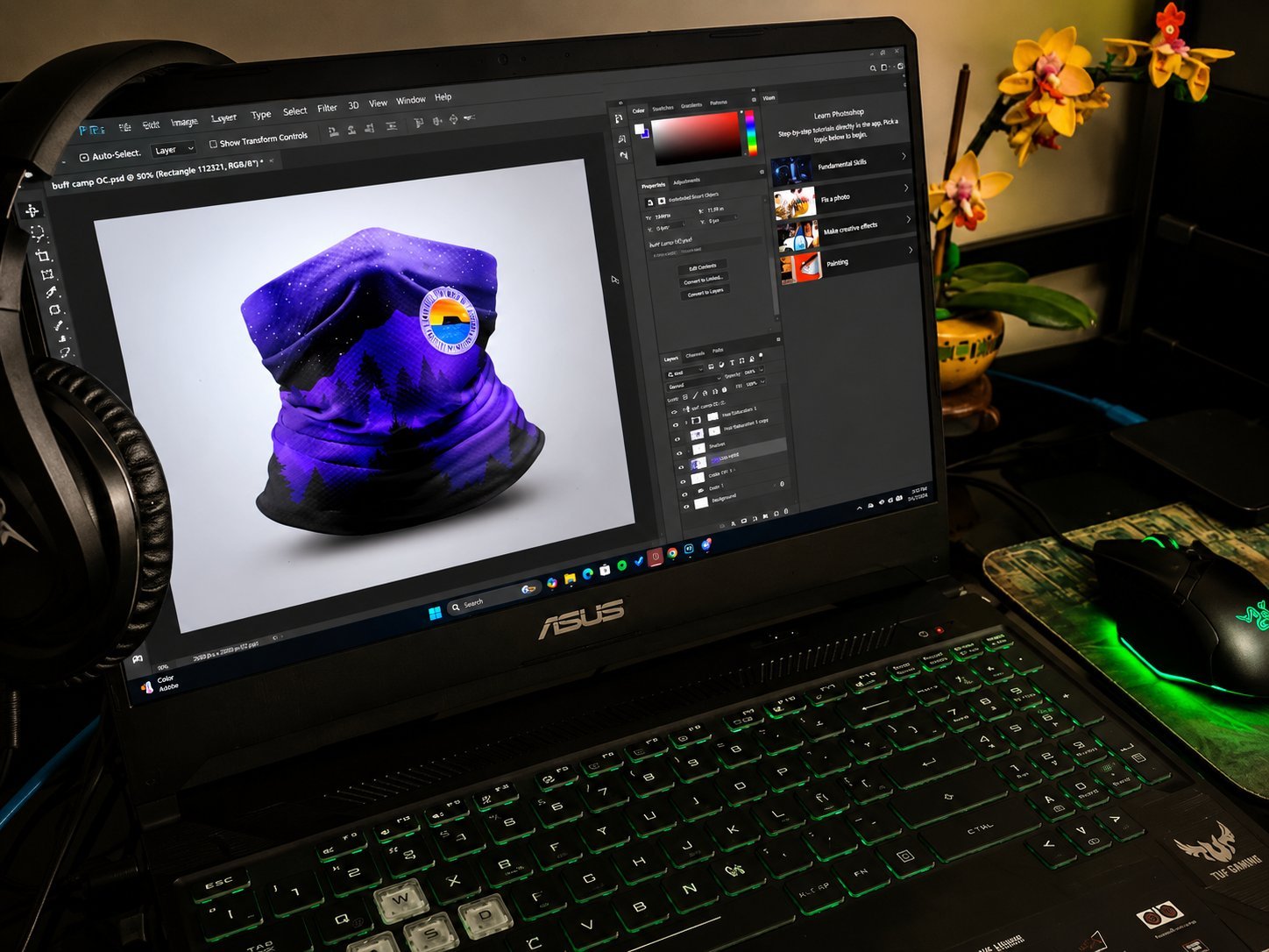 ASUS gaming laptop displaying 3D rendered purple fabric object in design software with headphones and mouse nearby