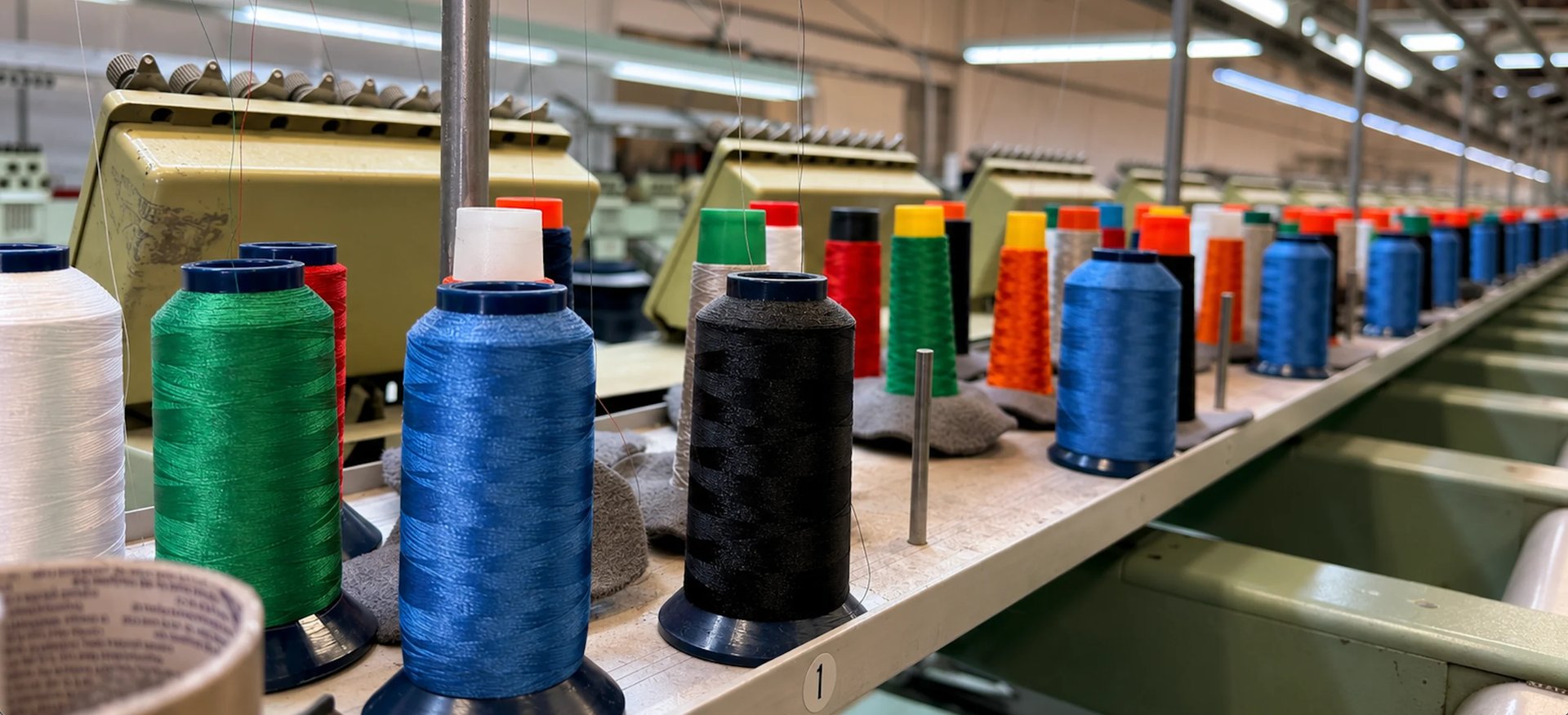 Large spools of colorful thread in a textile factory production line, arranged in rows under industrial lighting